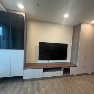 領袖特區電視牆收納設計：木紋基座結合白色系統門片，側邊配置黑玻璃展示櫃提升質感。